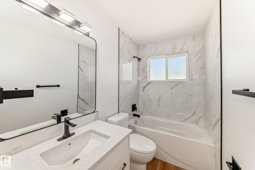 Bathroom featuring a white vanity with an integrated sink, a solid surface countertop, and a large mirror with a black frame - 4842 116Ave, Edmonton, AB - Indoor Photo Showing Bathroom