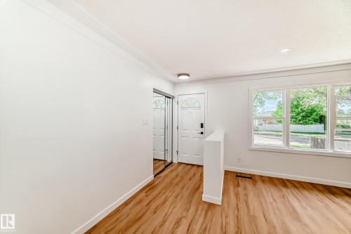 Bright entryway featuring wood-finish flooring, a white front door with decorative glass, and a mirrored sliding closet door - 4842 116Ave, Edmonton, AB - Indoor Photo Showing Other Room