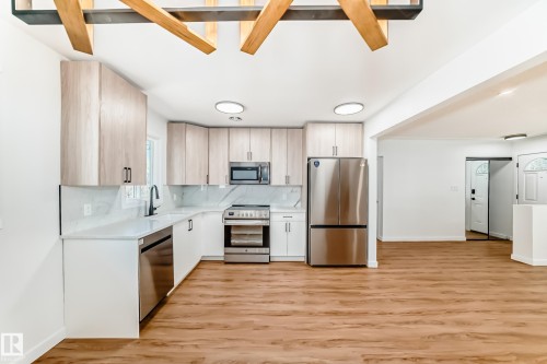 Modern kitchen featuring light wood-finish cabinetry, stainless steel appliances, white countertops, a white subway tile backsplash, and wood-finish flooring - 4842 116Ave, Edmonton, AB - Indoor Photo Showing Kitchen