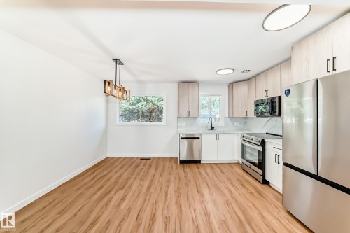 Contemporary kitchen featuring stainless steel appliances, light wood-finish cabinetry, white lower cabinets, and a white backsplash with grey veining - 4842 116Ave, Edmonton, AB - Indoor Photo Showing Kitchen