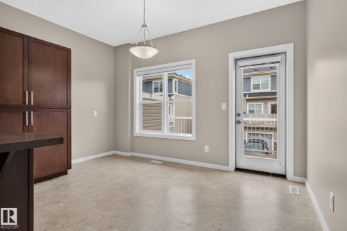 Dining area featuring a contemporary pendant light fixture, a large window with white trim, and a glass-paneled exterior door - 57 3710 Allan Drive, Edmonton, AB 