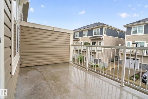 Private balcony featuring a durable concrete surface, beige horizontal siding, white railing, and exterior wall lighting - 57 3710 Allan Drive, Edmonton, AB 