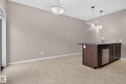 Kitchen island featuring a double-basin sink, stainless steel faucet, and integrated dishwasher - 57 3710 Allan Drive, Edmonton, AB 