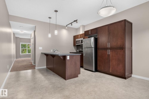 Kitchen featuring dark wood-finish cabinetry, stainless steel appliances, an island with a sink and pendant lighting, and light-toned flooring - 57 3710 Allan Drive, Edmonton, AB 