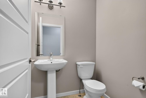 Pedestal sink with chrome faucet, rectangular mirror, and a three-light vanity fixture - 57 3710 Allan Drive, Edmonton, AB 