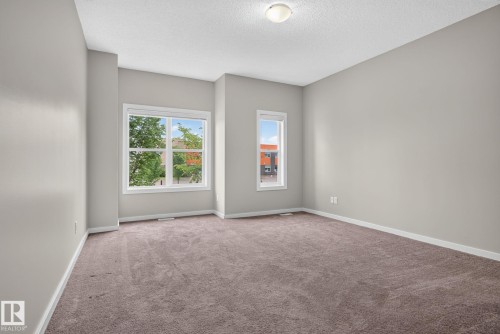 Spacious room featuring neutral painted walls, two windows with white trim, and plush carpeting - 57 3710 Allan Drive, Edmonton, AB 