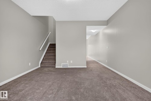 Carpeted room featuring a staircase with a white handrail, light gray painted walls, and white baseboards - 57 3710 Allan Drive, Edmonton, AB 