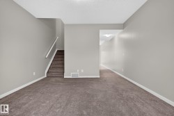 Carpeted room featuring a staircase with a white handrail, light gray painted walls, and white baseboards - 