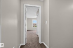 Hallway featuring neutral-toned walls, white trim, and brown carpet leading into a room with a window - 