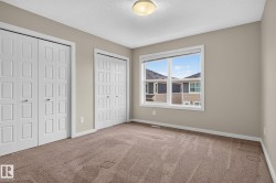 Carpeted room featuring a large window, neutral wall paint, two white bi-fold closet doors with square paneling, white trim, and a ceiling-mounted light fixture - 