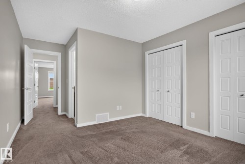 Neutral-toned interior room with plush carpet flooring, multiple bi-fold closet doors, and white trim - 57 3710 Allan Drive, Edmonton, AB 