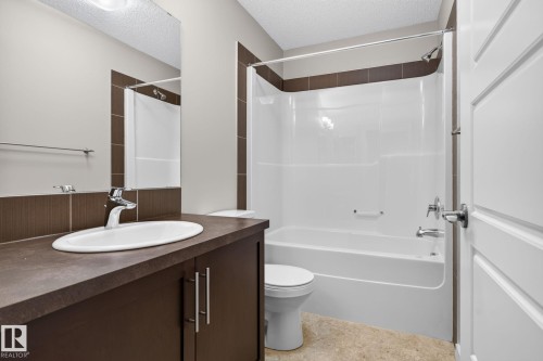 Bathroom featuring a white integrated tub and shower unit with chrome fixtures, a dark wood-finish vanity with an oval undermount sink, a large wall-mounted mirror, and neutral-toned wall and floor tiles - 57 3710 Allan Drive, Edmonton, AB 