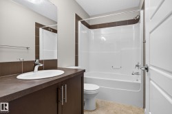 Bathroom featuring a white integrated tub and shower unit with chrome fixtures, a dark wood-finish vanity with an oval undermount sink, a large wall-mounted mirror, and neutral-toned wall and floor tiles - 