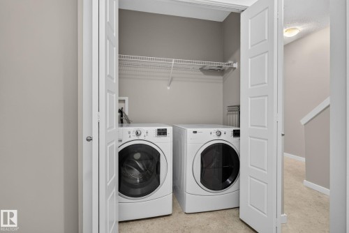 Dedicated laundry closet featuring a wire storage shelf, bi-fold doors, and neutral-toned flooring - 57 3710 Allan Drive, Edmonton, AB 