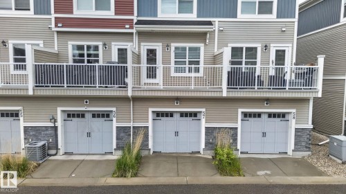 Exterior featuring light gray garage doors with decorative hardware, stone accents, and beige horizontal siding - 57 3710 Allan Drive, Edmonton, AB 