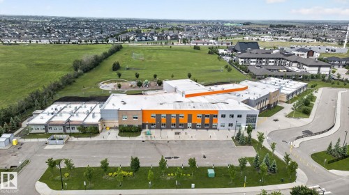 Modern institutional building with an orange and gray facade, extensive paved parking areas, and surrounding green spaces - 57 3710 Allan Drive, Edmonton, AB 