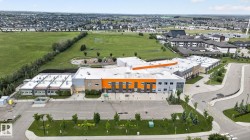 Modern institutional building with an orange and gray facade, extensive paved parking areas, and surrounding green spaces - 