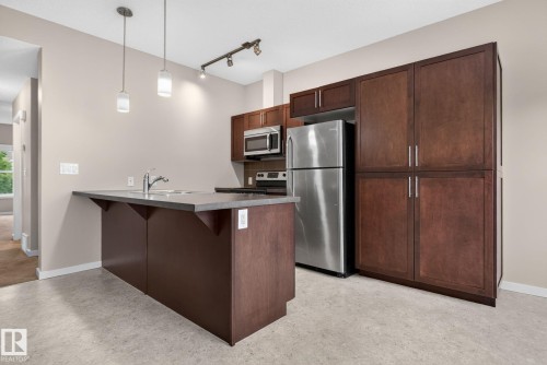 Kitchen featuring a center island with sink, stainless steel appliances, dark wood-finish cabinetry, and pendant lighting - 57 3710 Allan Drive, Edmonton, AB 