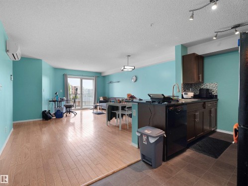 Open-concept living area featuring wood-finish flooring, a kitchen island with seating, dark wood cabinetry, and a sliding glass door leading to a balcony - 313 11820 22 Avenue, Edmonton, AB 
