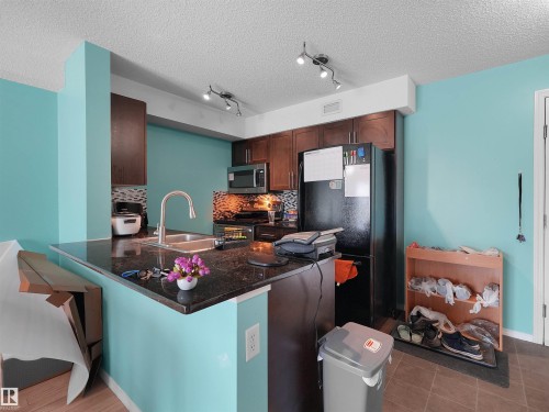 Kitchen featuring dark wood cabinetry, a built-in microwave, and a black refrigerator - 313 11820 22 Avenue, Edmonton, AB 