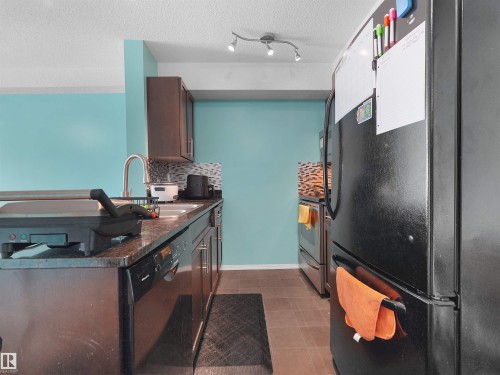Kitchen featuring dark cabinetry, granite-style countertops, and a tile backsplash - 313 11820 22 Avenue, Edmonton, AB 