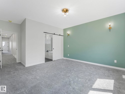 Spacious room featuring gray carpeting, a sage accent wall with sconce lighting, and a modern ceiling fixture - 1717 Crossbill Loop, Edmonton, AB - Indoor Photo Showing Other Room