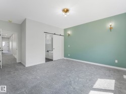 Spacious room featuring gray carpeting, a sage accent wall with sconce lighting, and a modern ceiling fixture - 