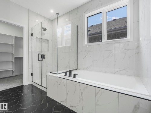 Bathroom featuring a built-in tub, separate glass-enclosed shower, black hexagon floor tiling, white marble-look wall tiling, and a window - 1717 Crossbill Loop, Edmonton, AB - Indoor Photo Showing Bathroom