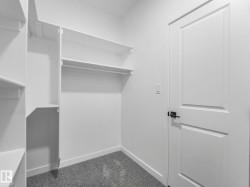 Walk-in closet featuring white built-in shelving, hanging rods, and grey carpeting - 