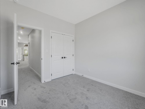 Carpeted interior room featuring light gray walls, white trim, and a double-door closet with dark hardware - 1717 Crossbill Loop, Edmonton, AB - Indoor Photo Showing Other Room