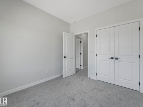 Light grey carpeted room featuring white trim, two panel doors with matte black hardware, and an additional doorway revealing a separate space - 1717 Crossbill Loop, Edmonton, AB - Indoor