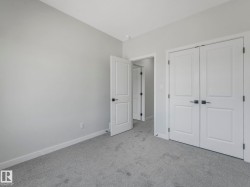 Light grey carpeted room featuring white trim, two panel doors with matte black hardware, and an additional doorway revealing a separate space - 
