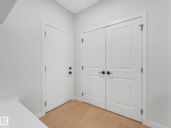 Entryway featuring wood-finish flooring, a white solid door with black hardware, and a double-door closet with black hardware - 