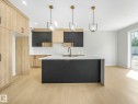 Kitchen featuring a large island with a waterfall countertop, light wood-finish flooring, two-tone cabinetry, marble-style backsplash, and three pendant lights - 1717 Crossbill Loop, Edmonton, AB  - Indoor Photo Showing Kitchen With Upgraded Kitchen 
