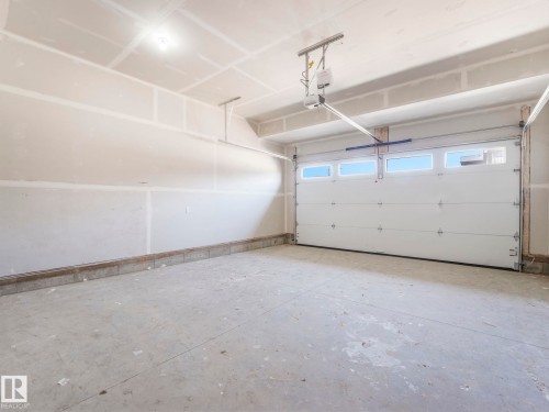 Spacious garage featuring a concrete floor, unpainted drywall, and a white paneled garage door with upper window inserts - 1717 Crossbill Loop, Edmonton, AB - Indoor Photo Showing Garage