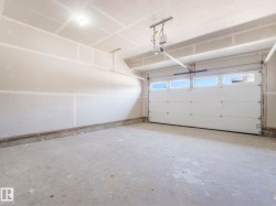 Spacious garage featuring a concrete floor, unpainted drywall, and a white paneled garage door with upper window inserts - 