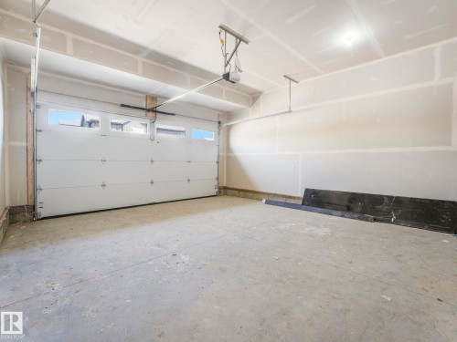 Spacious garage featuring a sectional overhead door with upper window panels, a concrete floor, and an automatic garage door opener - 1717 Crossbill Loop, Edmonton, AB - Indoor Photo Showing Garage