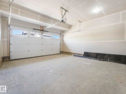 Spacious garage featuring a sectional overhead door with upper window panels, a concrete floor, and an automatic garage door opener - 