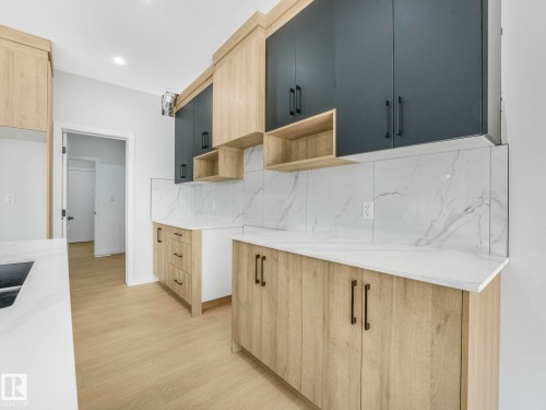 Modern kitchen featuring light wood-finish lower cabinetry, dark gray upper cabinetry with bronze hardware, and white countertops - 1717 Crossbill Loop, Edmonton, AB - Indoor Photo Showing Kitchen With Double Sink