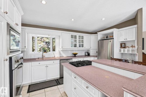 White kitchen cabinetry with a bay window, recessed lighting, integrated stainless steel appliances, a gas cooktop, and a kitchen island with a raised breakfast bar - 860 41 Avenue, Edmonton, AB 
