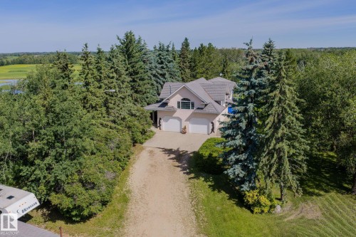 Stucco exterior residence featuring a multi-car garage, mature evergreen trees, expansive green space, and a paved driveway - 860 41 Avenue, Edmonton, AB 