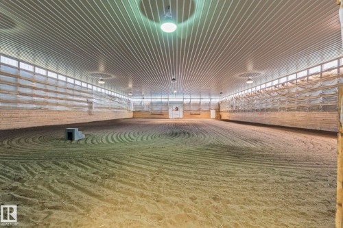 Spacious indoor arena featuring a sand footing, corrugated metal ceiling, perimeter wood paneling, extensive translucent paneling for natural light, and overhead lighting fixtures - 860 41 Avenue, Edmonton, AB 