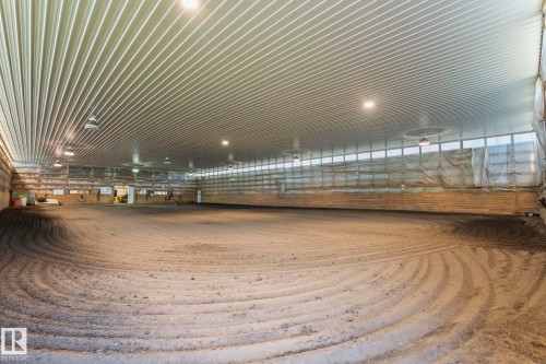 Spacious indoor arena featuring a prepared sand footing, high corrugated metal ceiling, perimeter windows, and multiple overhead light fixtures - 860 41 Avenue, Edmonton, AB 