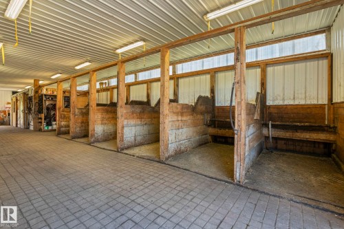 Barn interior featuring a corrugated metal ceiling, wood-framed stalls with metal siding, and a paved brick-patterned aisle - 860 41 Avenue, Edmonton, AB 
