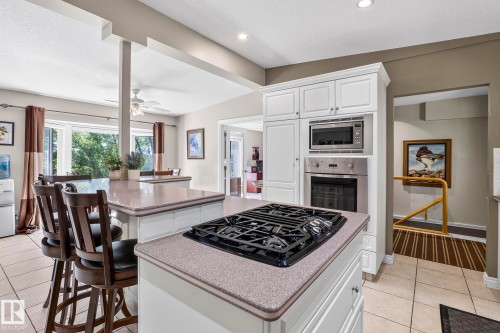 Kitchen featuring a gas cooktop on a central island, built-in stainless steel microwave and oven, white cabinetry, and light-toned countertops - 860 41 Avenue, Edmonton, AB 
