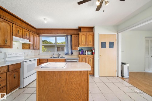 Kitchen featuring wood cabinetry, white appliances, a central island, tile flooring, and a ceiling fan - 14916 114A Street, Edmonton, AB 