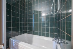 Bathtub and shower combination featuring dark green square tiles with light grout and chrome fixtures - 