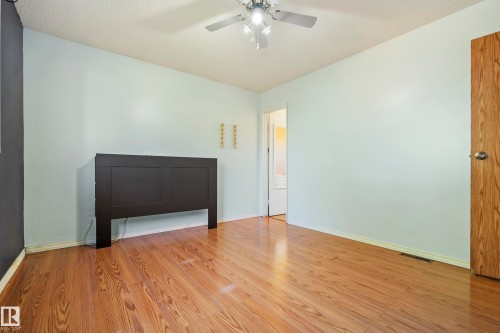 Room featuring wood-finish flooring, light blue and dark gray wall finishes, a ceiling fan with integrated lighting, and a wood-paneled door - 14916 114A Street, Edmonton, AB 