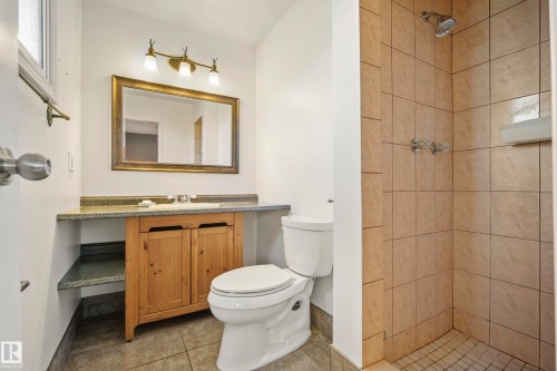 Bathroom featuring a wood-finish vanity with a built-in sink, a framed mirror, and a three-light fixture - 14916 114A Street, Edmonton, AB 
