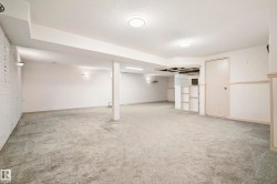 Spacious lower-level room featuring light gray carpeting, recessed ceiling lighting, and a partially finished built-in bar area with shelving - 